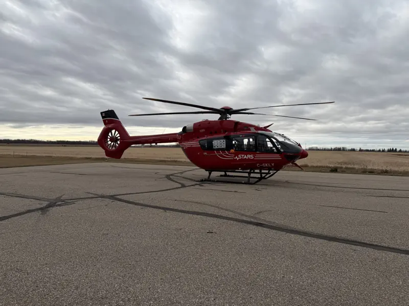 A red medical helicopter on a wet apron under heavy cloud
