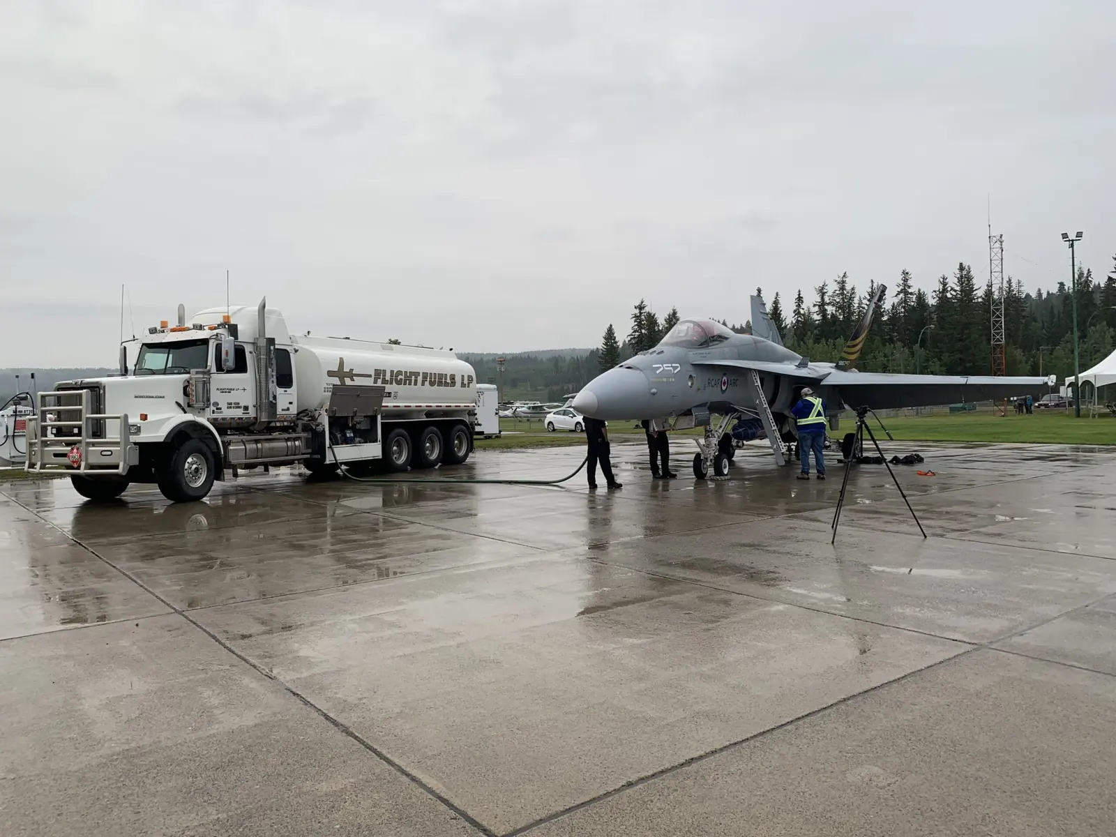 A Flight Fuels tanker truck refuelling a fighter jet on a wet apron while the ground crew works under the wing