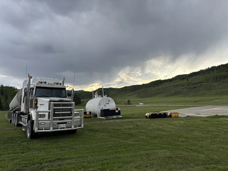 A Flight Fuels tanker truck parked beside a storage tank on a grass airstrip in the foothills